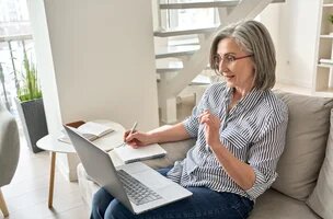 Femme d'environ 60 ans assise sur un canapé et travaillant sur son ordinateurportable